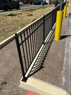 Angled black picket fence mounted on a low concrete wall beside a parking area