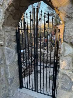 Angled view of a narrow black gate beneath a rough stone arch