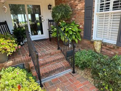 Angled view of black railings on brick steps beside lush porch plants