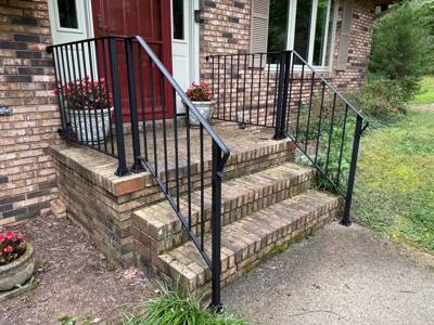 Angled view of black railings on short brick-and-stone porch steps