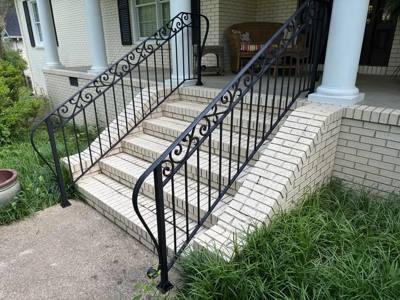 Angled view of black scrollwork stair railings at a columned brick porch