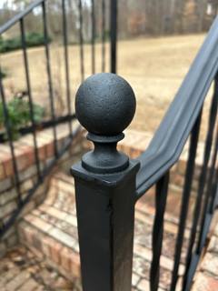 Ball finial and curved handrail end above black picket balusters