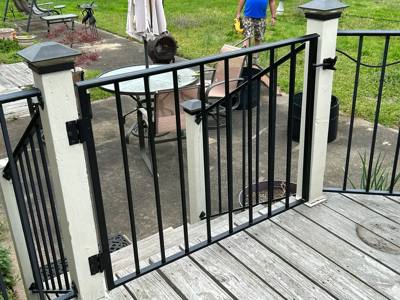 Black deck gate with vertical pickets and a latch beside pale posts
