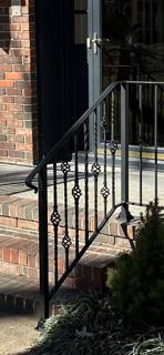 Black decorative railing at a shaded brick entrance