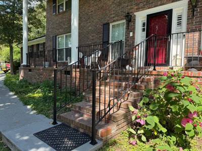 Black decorative railings on brick porch steps beside flowering plants