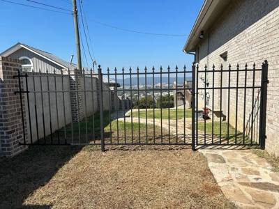 Black double gate between a brick wall and a light-colored building