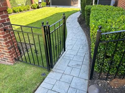 Black fence and pedestrian gate bordering a curved paved garden path