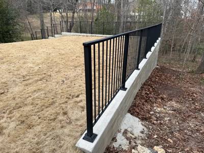 Black fence panels mounted along a white retaining wall