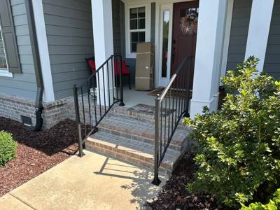 Black handrails at a small brick stoop on a gray-sided porch