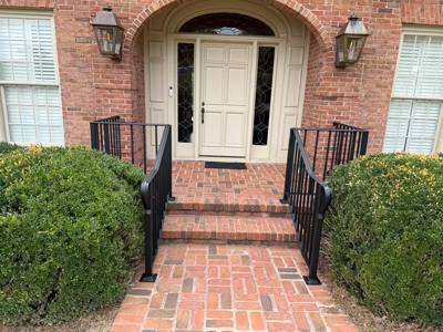 Black handrails at short brick steps leading to a white front door