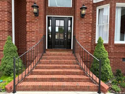 Black handrails beside a broad brick stairway to dark double doors