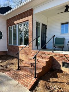 Black handrails beside brick steps at a white-sided corner porch