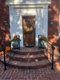 Black handrails beside curved brick steps at an ornate front doorway