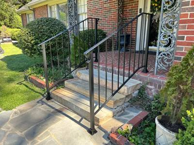 Black handrails beside stone entry steps and a planted garden