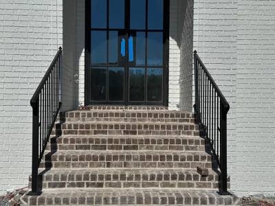 Black handrails flanking brick steps beneath a tall arched entrance