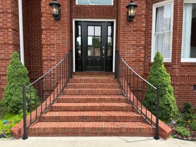 Black handrails flanking broad brick stairs to double entry doors