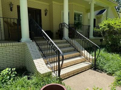Black handrails flanking white brick stairs at a covered porch