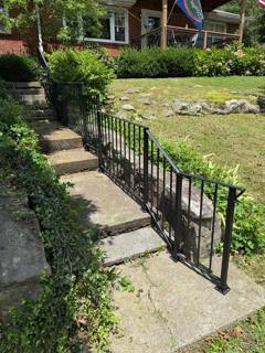 Black handrails following garden steps between shrubs and a stone wall