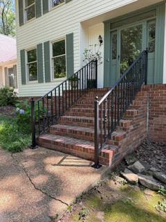 Black handrails following tall brick stairs to a white-columned porch