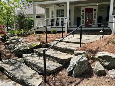 Black handrails following uneven stone garden steps toward a covered porch