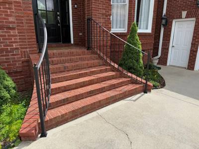 Black handrails framing broad brick steps beside evergreen shrubs