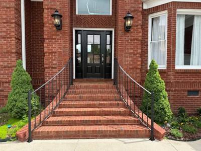 Black handrails lining a broad brick staircase to double entry doors