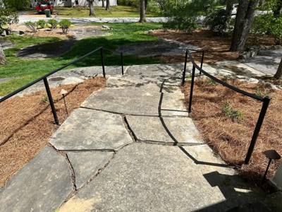 Black handrails lining a broad stone walkway through a wooded garden