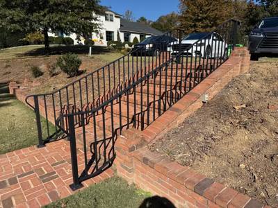 Black handrails on brick steps beside a broad landscaped slope