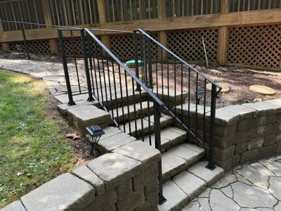 Black handrails on stone steps through a low retaining wall