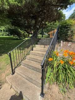 Black handrails running up a long outdoor concrete stairway beside flowers