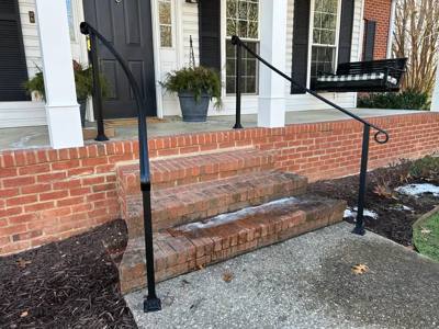 Black handrails with curled ends beside brick porch steps