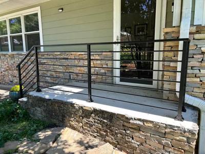Black horizontal railing around a small porch above a stone foundation