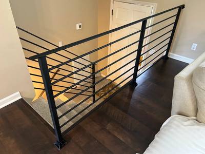 Black horizontal railing around an interior stair opening with dark wood flooring