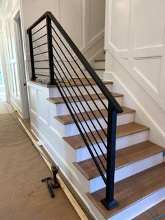 Black horizontal railing beside pale wooden interior stairs and a white door