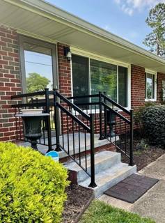 Black horizontal railings on concrete steps beside a brick house