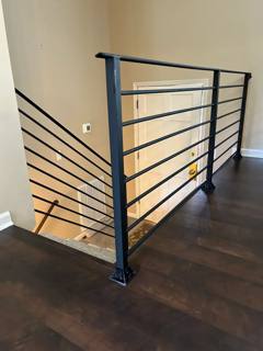 Black horizontal stair guardrail beside pale interior walls and dark wood flooring