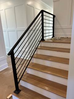 Black horizontal stair railing ascending beside paneled white interior walls