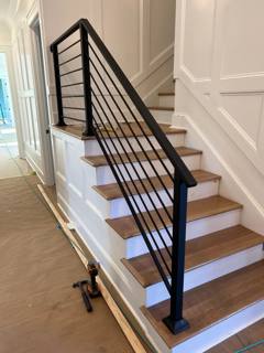 Black horizontal stair railing beside pale wooden interior treads