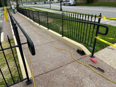 Black loop-ended handrail beside a long sloping paved walkway