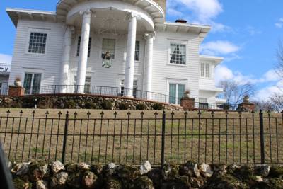 Black ornamental fence across the lawn of a white columned house