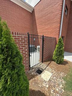 Black pedestrian gate beside a brick wall and planted shrubs