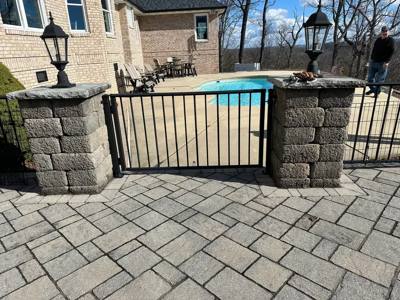 Black pedestrian gate between stone pillars beside a swimming pool