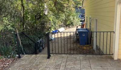 Black pedestrian gate closing a paved side passage beside pale siding