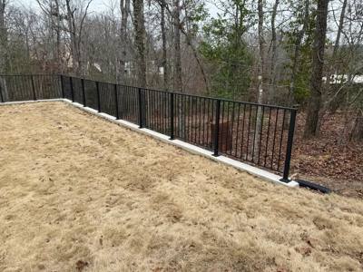 Black picket fence along the edge of a wooded lawn