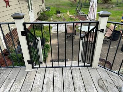 Black picket gate between pale posts on a wooden deck