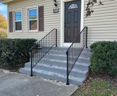 Black picket handrails framing gray entry steps beside shrubs