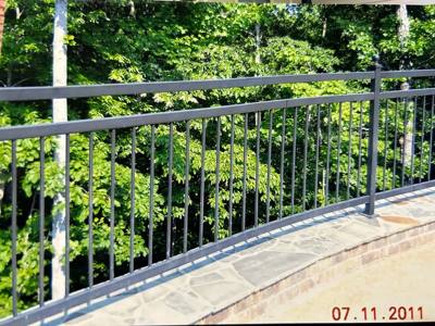 Black picket railing above a stone terrace beside dense green trees