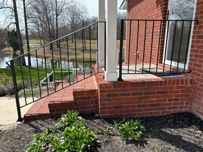 Black picket railing beside a brick porch and sloping steps