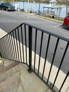 Black picket railing beside outdoor entrance steps and a paved parking area