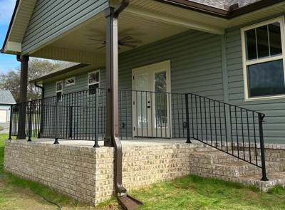 Black picket railing enclosing a raised covered porch with pale siding